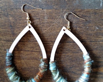 May include: A pair of teardrop-shaped earrings with a white wooden base wrapped in colorful yarn. The yarn is a mix of blue, green, brown, and white.