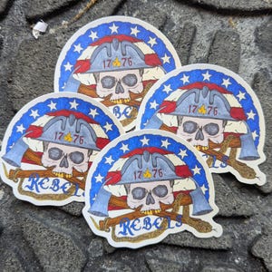 May include: Four stickers with a patriotic design. Each sticker features a skull wearing a firefighter's helmet, crossed axes, and the text "1776" and "Rebels". The design incorporates red, white, and blue colours, with a star-studded border.