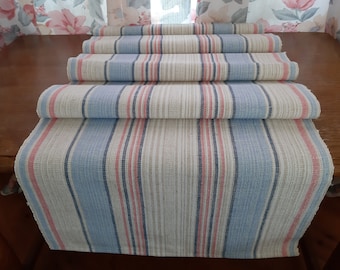 May include: A set of striped table runners in shades of blue, pink, and beige. The runners are woven with a textured pattern and have a natural, rustic look.