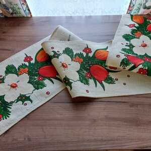 Può includere: Due runner da tavolo in lino bianco con un design floreale con tulipani rossi e arancioni, foglie verdi e fiori bianchi. I runner sono su una superficie di legno.