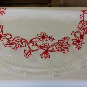 May include: White round tablecloth with a red embroidered floral design and a white crocheted lace trim.
