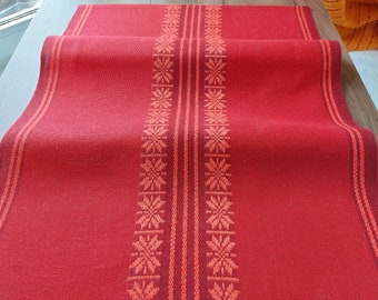 Può includere: Tovaglia da tavolo rossa con un design intrecciato che presenta un motivo ripetitivo di stelle arancioni. La tovaglia è piegata a metà e ha una superficie testurizzata.
