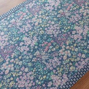 Könnte beinhalten: Ein blauer Tischläufer mit einem Blumenmuster mit rosa, weißen und gelben Blumen. Der Läufer hat einen weißen Rand mit einem kleinen, sich wiederholenden Muster.
