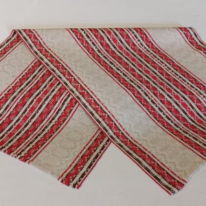 May include: A white fabric table runner with red and brown stripes. The runner has a woven pattern and is folded in half.