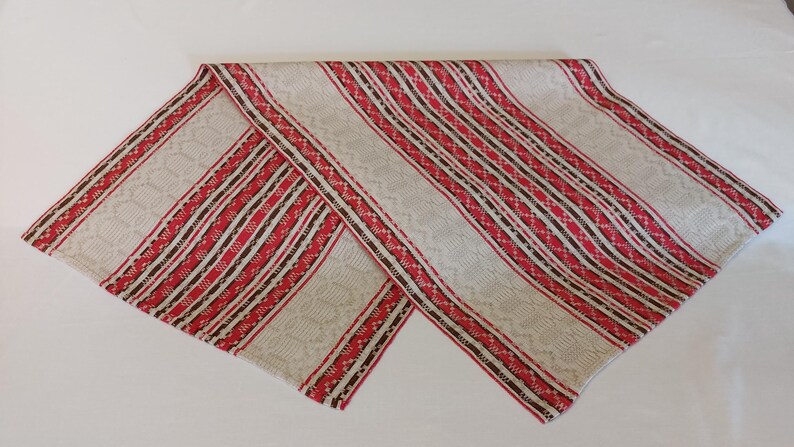May include: A white fabric table runner with red and brown stripes. The runner has a woven pattern and is folded in half.