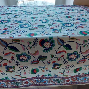 May include: White tablecloth with a floral pattern in shades of blue, green, red, and pink. The tablecloth has a border with a repeating pattern of flowers and leaves.