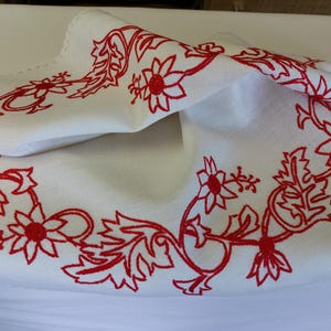 May include: White linen tablecloth with a red embroidered floral design. The design features stylised flowers and leaves.