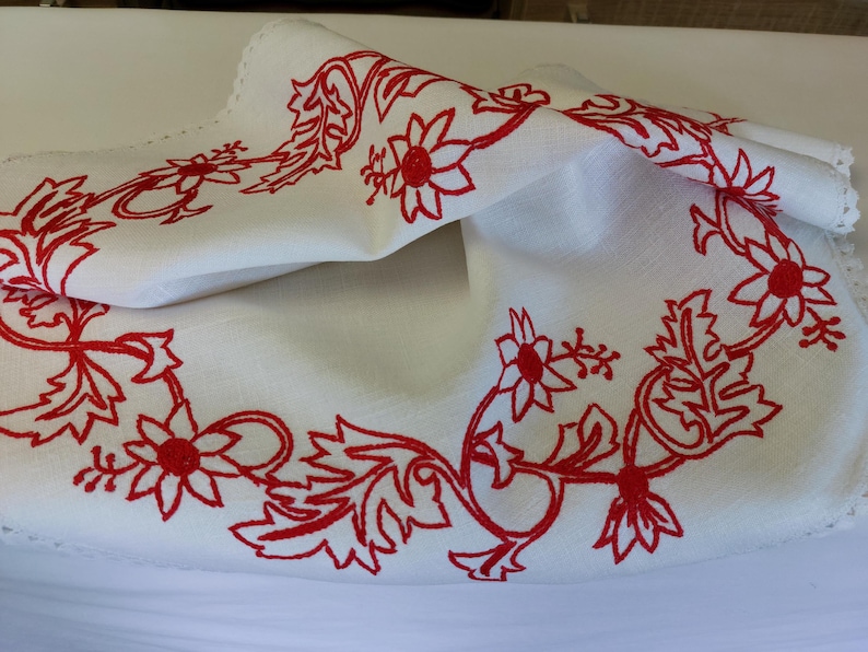 May include: White linen tablecloth with a red embroidered floral design. The design features stylised flowers and leaves.