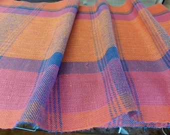 May include: Close-up of a woven fabric with a plaid pattern in shades of orange, red, and blue.