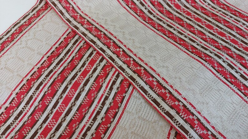 May include: Red and brown striped fabric with a white background. The fabric has a woven pattern.
