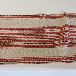 May include: A beige fabric with red, brown, and white stripes. The fabric has a woven pattern and is suitable for upholstery or crafting projects.