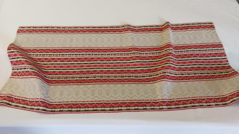 May include: A beige fabric with red, brown, and white stripes. The fabric has a woven pattern and is suitable for upholstery or crafting projects.