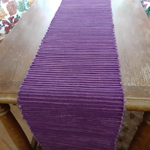 May include: A purple table runner with a ribbed texture. The runner is made of a woven material and has a subtle sheen.