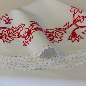May include: White tablecloth with a red floral embroidery design and a white lace trim.