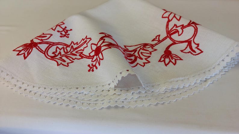 May include: White tablecloth with a red floral embroidery design and a white lace trim.