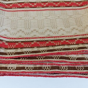 May include: A folded fabric tablecloth with a white background and brown and red stripes. The tablecloth has a woven pattern.