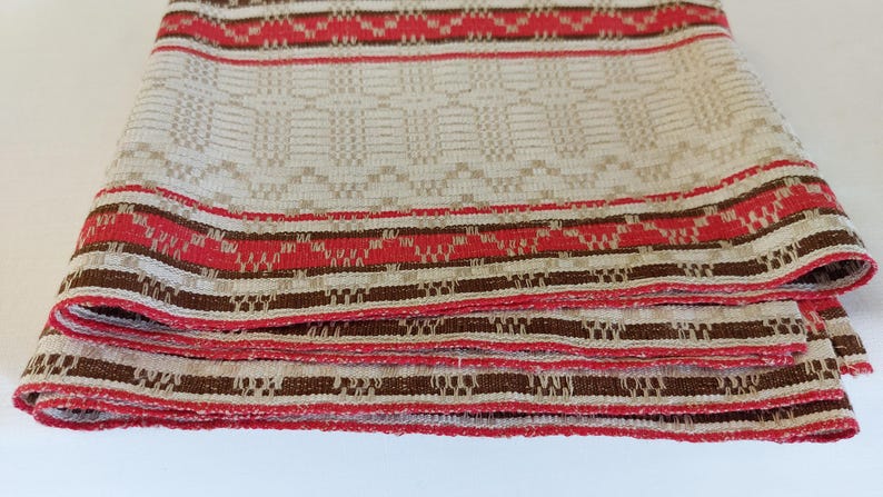May include: A folded fabric tablecloth with a white background and brown and red stripes. The tablecloth has a woven pattern.