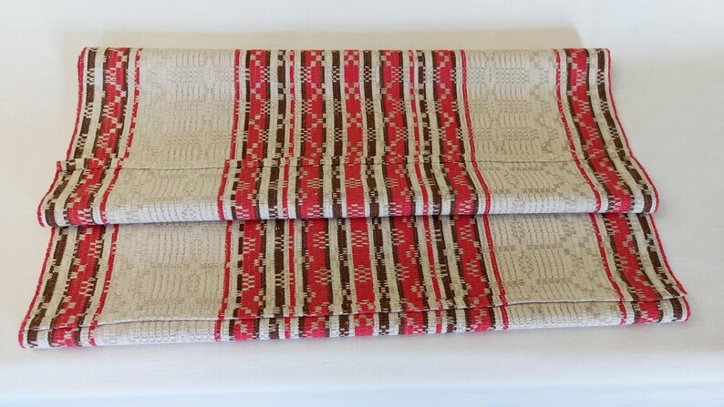 May include: A beige table runner with red and brown stripes and a geometric pattern.
