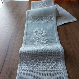May include: White crocheted table runner with a floral design and a repeating pattern of the word "Love".