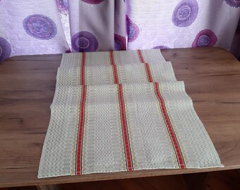 May include: A white table runner with red and black stripes. The runner is made of a woven fabric and has a textured surface.