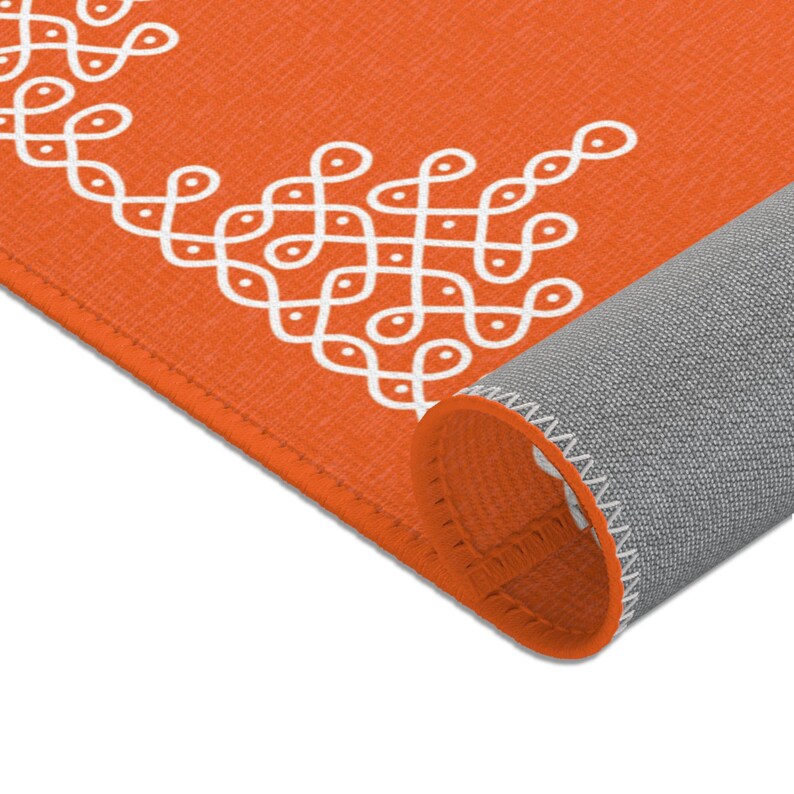 May include: Orange rug with a white geometric pattern. The rug is rolled up, showing the gray backing and white stitching.