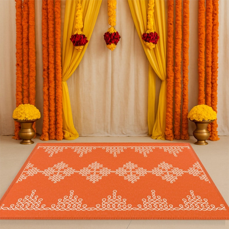 May include: An orange and white patterned rug with a traditional Indian design. The rug is placed in front of a backdrop of yellow and orange flower garlands and white curtains.