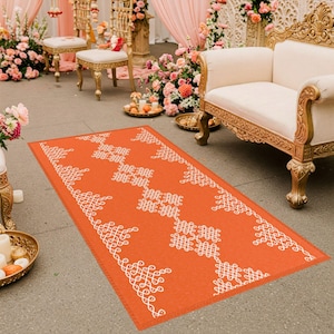 May include: An orange and white patterned runner rug with a traditional Indian design. The rug is laid out on a floor in front of two chairs and a couch.