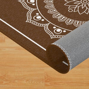 May include: A brown rug with a white mandala design. The rug is rolled up and the edge of the rug is visible.