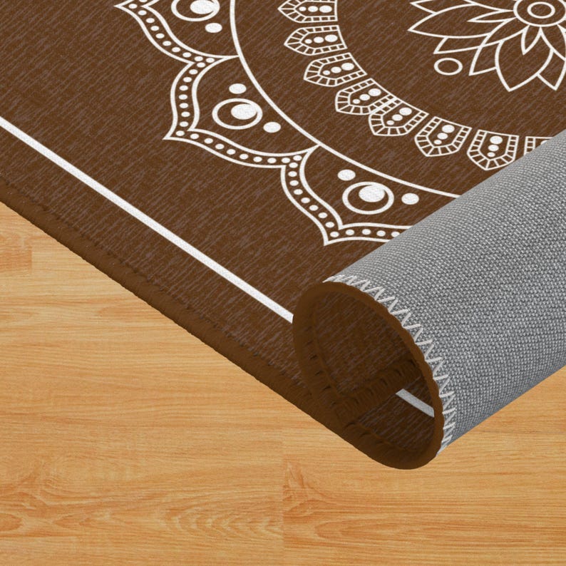 May include: A brown rug with a white mandala design. The rug is rolled up and the edge of the rug is visible.