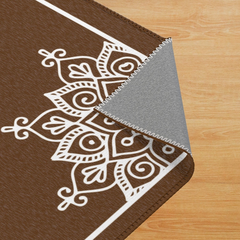 May include: A brown and white area rug with a white mandala design. The rug has a white border and a brown background.