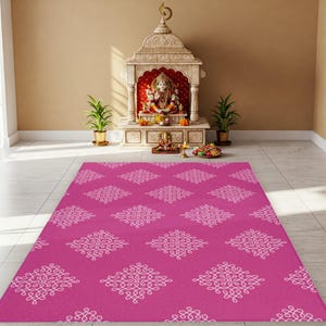May include: A pink prayer rug with a white geometric pattern. The rug is in front of a small, ornate shrine with a statue of a deity.