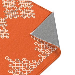 May include: Orange throw rug with a white geometric pattern. The rug has a fringed edge and is folded in half.