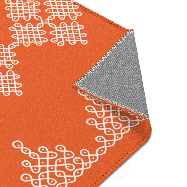 May include: Orange throw rug with a white geometric pattern. The rug has a fringed edge and is folded in half.