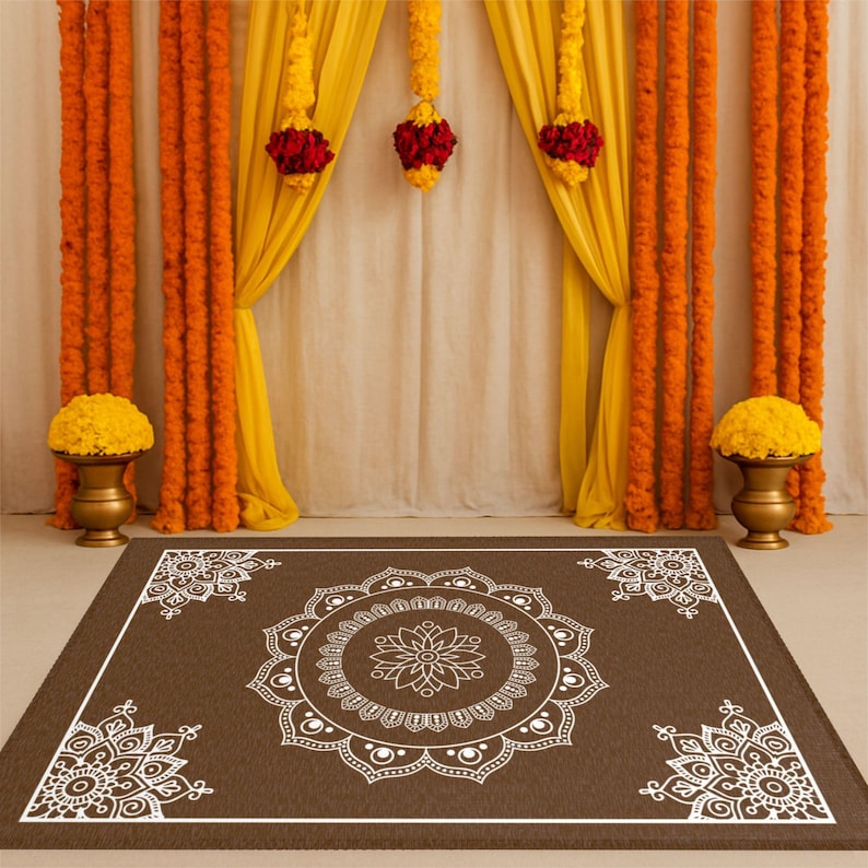 May include: A brown square rug with a white mandala design in the center and smaller mandalas in each corner. The rug is in front of a backdrop of yellow and orange fabric drapes.