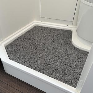 Könnte beinhalten: Eine graue, strukturierte Matte in einer weißen Duschkabine. Die Matte ist so geformt, dass sie in die Ecke der Dusche passt, mit einer abgerundeten Kante. Die Oberfläche der Matte hat ein dichtes, geschlungenes Muster.