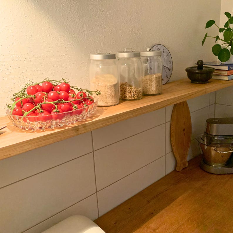 K&ouml;nnte beinhalten: Ein K&uuml;chenregal aus Holz zeigt eine Glasschale mit roten Kirschtomaten, drei Gl&auml;ser mit silbernen Deckeln und einen kleinen schwarzen M&ouml;rser und St&ouml;&szlig;el. Eine Uhr und eine Pflanze sind ebenfalls zu sehen.