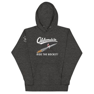 May include: A dark gray hooded sweatshirt with a white graphic of a rocket with a person sitting on top. The text "Oldsmobile" is above the rocket and "Ride the Rocket!" is below the rocket. There is a small logo on the left sleeve that says "Black Yacht".