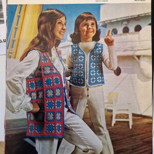 Può includere: Copertina di un modello vintage all'uncinetto con due persone che indossano gilet all'uncinetto. I gilet hanno un motivo quadrato blu e rosso. La copertina include il testo "Broute Regd" e "Double Knitting Crochet". Il modello è per un bolero e una giacca.