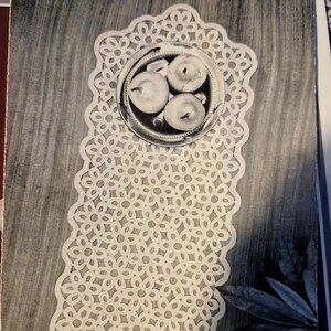 Puede incluir: Doily de crochet blanco con un patrón floral. El doily está colocado sobre una superficie de madera y tiene un tazón con tres manzanas.