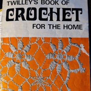 Könnte beinhalten: Ein Vintage-Buch mit dem Titel "Twilley's Book of Crochet for the Home" mit einem Cover, das ein weißes Häkelmuster auf orangefarbenem Hintergrund zeigt. Der Text "Contents Illustrated on Back Cover" ist unten auf dem Cover gedruckt.