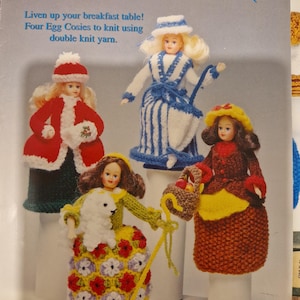 Może przedstawiać: Okładka książki "Four Little Seasons" z czterema osłonkami na jajka w kształcie lalek. Osłonki są w kolorach czerwonym, niebieskim i żółtym, ze szczegółami takimi jak kapelusze i płaszcze. Tekst brzmi "Liven up your breakfast table! Four Egg Cosies to knit using double knit yarn."