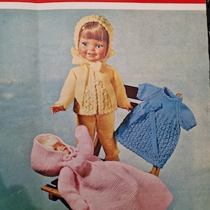 May include: A vintage Bronte knitting pattern for dolls' clothes. The image shows a doll in a yellow knitted outfit and bonnet, a blue knitted dress, and a pink hooded blanket. The pattern is for double knitting and is marked with the number 764.