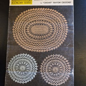 May include: Vintage Homecraft crochet pattern booklet featuring three lace crochet mat designs. The cover displays a large oval mat and two smaller circular mats in shades of beige and blue-green. The text reads "Luncheon or Cheval Lace Crochet Mats".