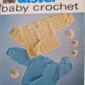 May include: A crochet pattern for a baby cardigan. The pattern includes instructions for two different styles: a yellow cardigan with a lacy stitch and a blue cardigan with a textured stitch. The pattern is from Lister and is number N2521.