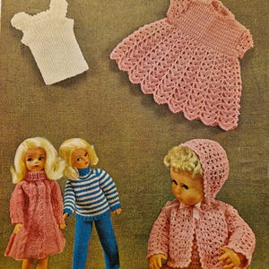 May include: A crochet pattern for a doll outfit, featuring a pink dress, a pink sweater and pants set, and a pink hat and booties set. The pattern is from Wendy, 4 ply's, and the pattern number is 893.