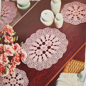 May include: Four pink crochet doilies with a floral design. The doilies are on a wooden table with a vase of pink roses. The text on the page reads "Mercer Crochet Cotton no. 40 CROCHET no. 871".