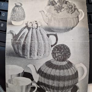 May include: A vintage black and white image featuring three tea cosies, each with a unique knitted design. The image also includes a matching egg cosy and text that reads "THREE TEA-COSIES".