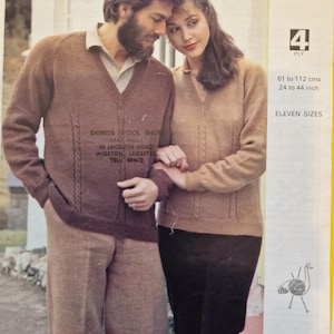 Puede incluir: Una pareja lleva jerséis de punto marrón con un patrón de trenza. El hombre lleva pantalones marrones y la mujer lleva pantalones negros. Los jerséis tienen una etiqueta que dice "Doris's Wool Shop (Pat Hall) 50 Leicester Road Wigston, Leicester Tel 884410". La imagen también incluye una etiqueta con el texto "Stephen 4815 Emu 4 Ply 61 a 112 cm 24 a 44 pulgadas Once tallas".