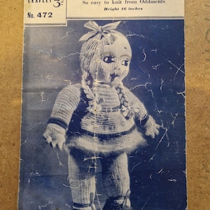 Puede incluir: Folleto de patrón de tejido vintage titulado 'Dolly Dimples' con una muñeca tejida. La muñeca lleva un vestido y zapatos, con un lazo en el pelo. El folleto es azul y blanco, la muñeca mide 40.6 cm.