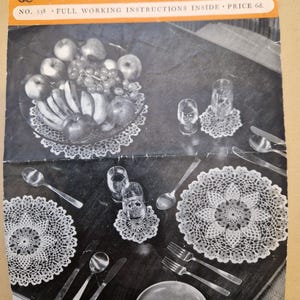 Könnte beinhalten: Vintage Häkelanleitungsheft mit dem Text "COATS Mercer-Crochet Design". Das Bild zeigt eine Tischdekoration mit gehäkelten Deckchen, Glaswaren, Besteck und einem Obstteller. Das Heft hat die Nummer 538.